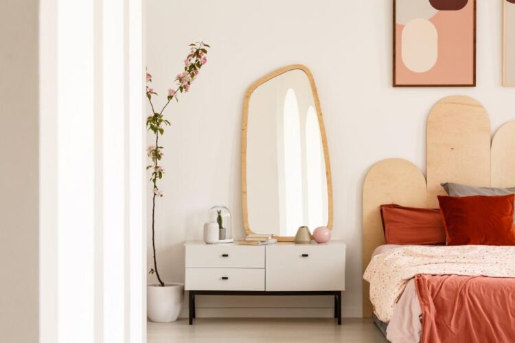 Plant next to white dressing table with mirror in red bedroom apartment interior with poster above bed.